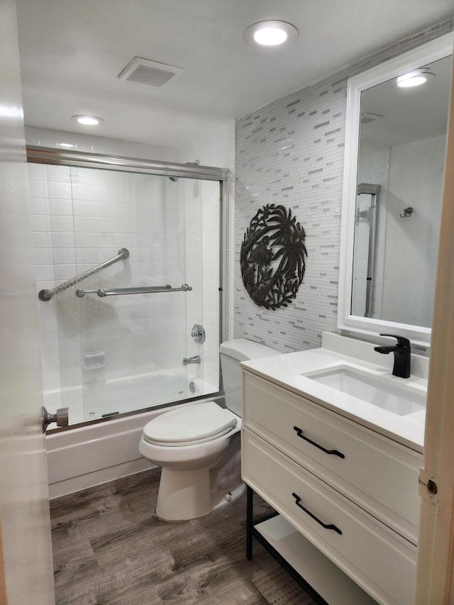 full bathroom with hardwood / wood-style floors, vanity, bath / shower combo with glass door, and toilet