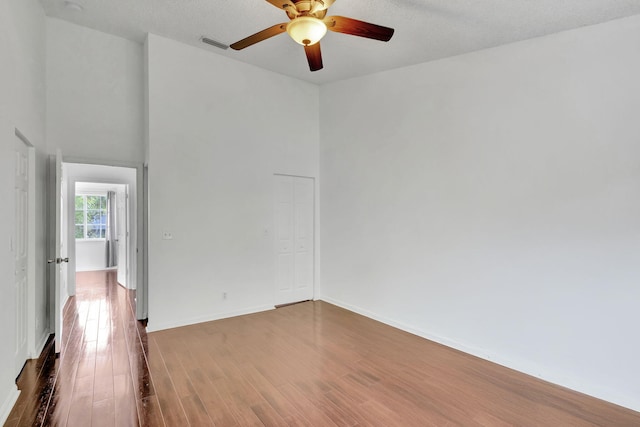 unfurnished room featuring ceiling fan, a high ceiling, a textured ceiling, and hardwood / wood-style flooring