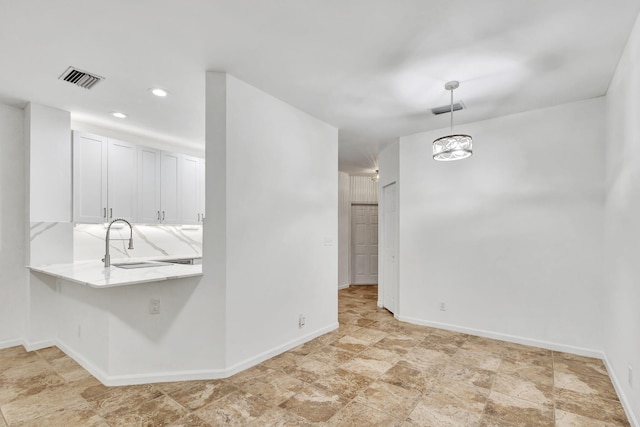 kitchen with kitchen peninsula, sink, white cabinets, and decorative light fixtures