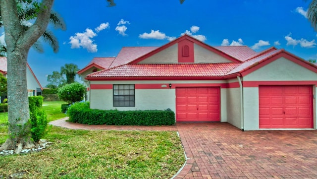 view of front of property with a tile roof, a front yard, stucco siding, decorative driveway, and a garage