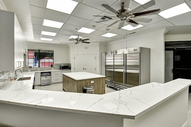 kitchen featuring built in refrigerator, light stone countertops, a center island, sink, and kitchen peninsula