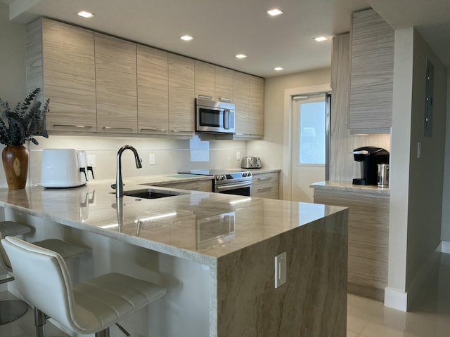 kitchen featuring kitchen peninsula, a kitchen breakfast bar, light stone counters, stainless steel appliances, and sink