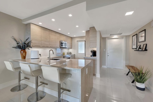 kitchen featuring sink, appliances with stainless steel finishes, light stone counters, a kitchen bar, and kitchen peninsula