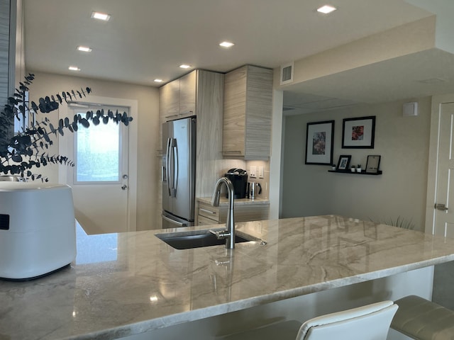 kitchen featuring a kitchen breakfast bar, sink, stainless steel fridge, light stone counters, and kitchen peninsula