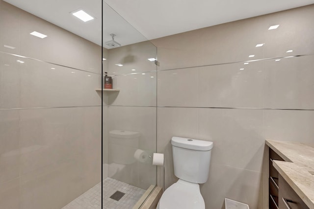 bathroom with vanity, a tile shower, tile walls, and toilet