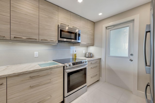 kitchen with light brown cabinets, appliances with stainless steel finishes, light tile patterned floors, and light stone counters