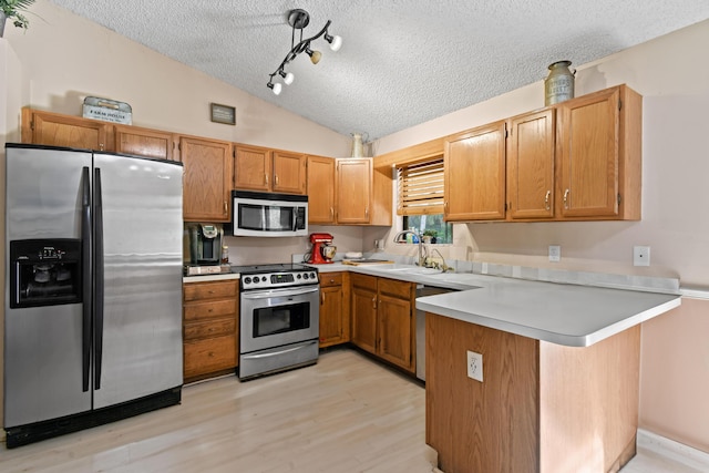 kitchen with kitchen peninsula, a textured ceiling, stainless steel appliances, vaulted ceiling, and light hardwood / wood-style floors