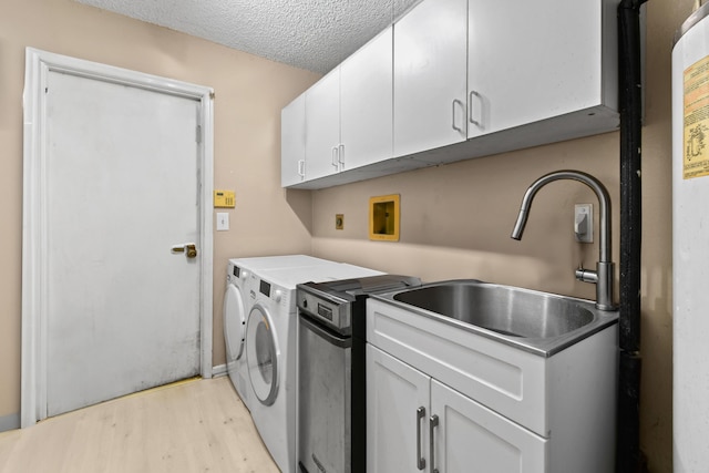 washroom with cabinets, sink, a textured ceiling, light hardwood / wood-style floors, and washing machine and clothes dryer