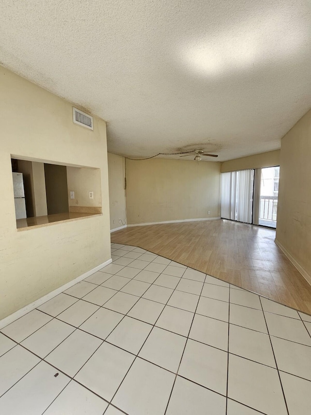 empty room featuring a textured ceiling, visible vents, baseboards, a ceiling fan, and light wood finished floors