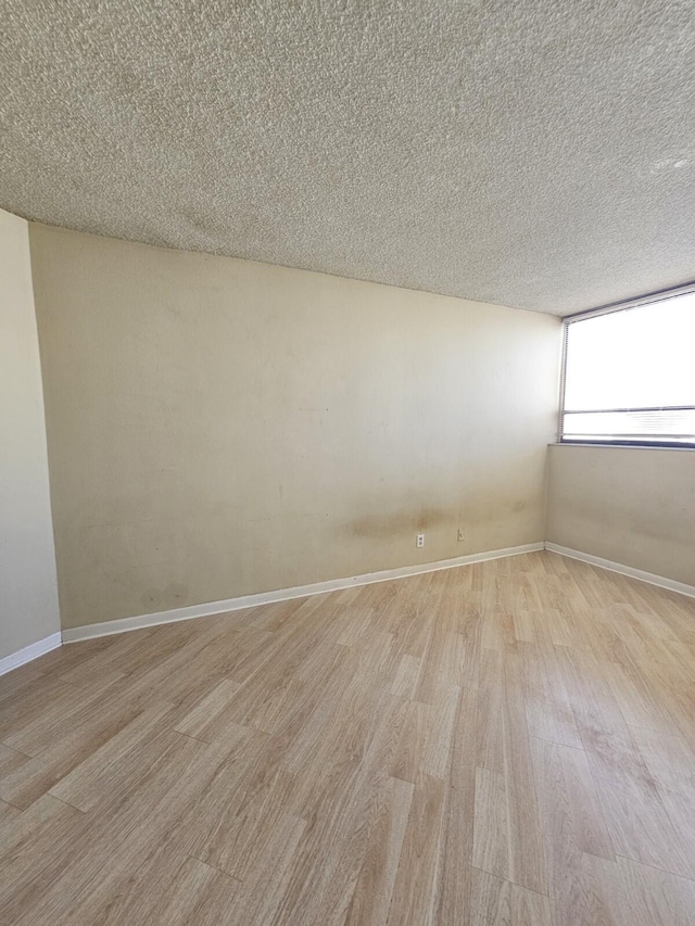 empty room featuring a textured ceiling, baseboards, and light wood-style floors