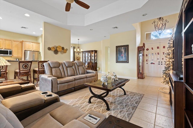 living room featuring light tile patterned floors, ceiling fan with notable chandelier, and a tray ceiling