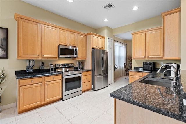 kitchen with light brown cabinets, dark stone counters, sink, light tile patterned floors, and appliances with stainless steel finishes