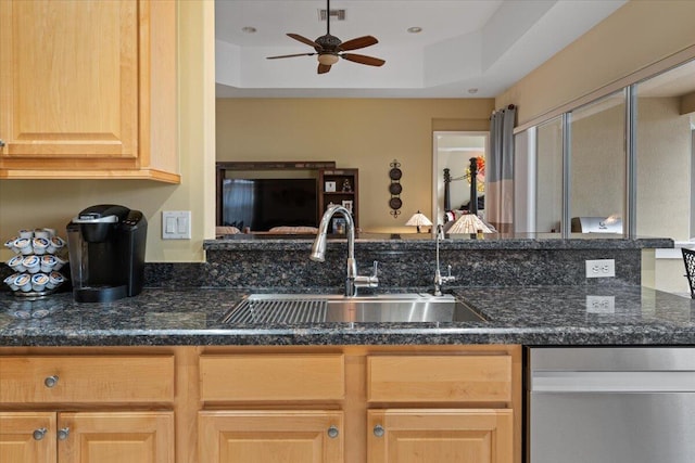 kitchen featuring ceiling fan, sink, a raised ceiling, dark stone countertops, and light brown cabinetry