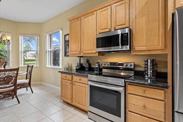 kitchen with dark stone countertops, an inviting chandelier, light tile patterned floors, and appliances with stainless steel finishes