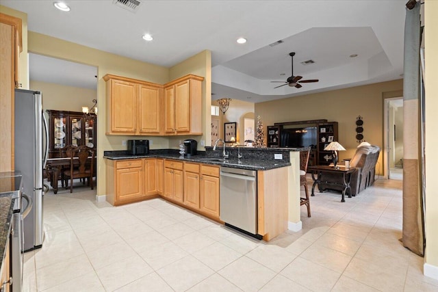 kitchen featuring kitchen peninsula, dark stone counters, stainless steel appliances, a tray ceiling, and ceiling fan