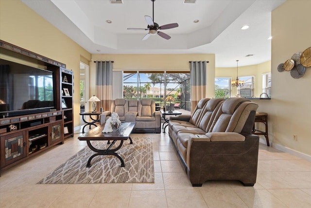 living room featuring a tray ceiling, light tile patterned floors, and ceiling fan with notable chandelier