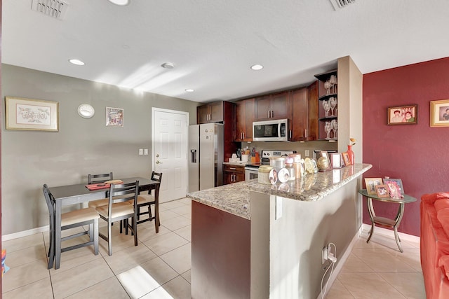 kitchen featuring light stone countertops, a kitchen bar, kitchen peninsula, stainless steel appliances, and light tile patterned floors