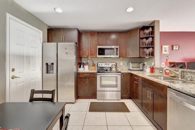 kitchen with sink, light tile patterned floors, a textured ceiling, light stone countertops, and appliances with stainless steel finishes