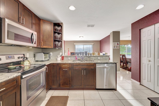 kitchen featuring sink, light stone counters, kitchen peninsula, stainless steel appliances, and a chandelier