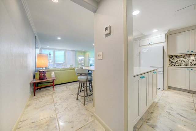 kitchen featuring white cabinetry, ornamental molding, a kitchen breakfast bar, and white refrigerator