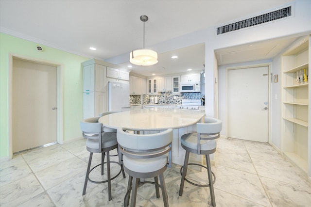 kitchen with white appliances, a breakfast bar, white cabinetry, hanging light fixtures, and decorative backsplash