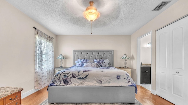 bedroom with ceiling fan, light hardwood / wood-style flooring, ensuite bathroom, a textured ceiling, and a closet