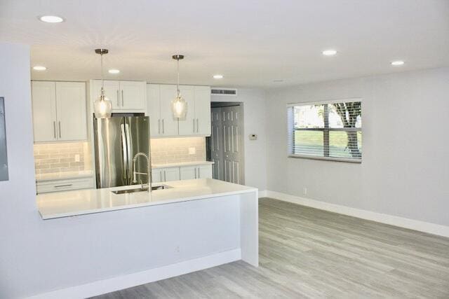 kitchen featuring white cabinets, stainless steel fridge, light wood-type flooring, and pendant lighting