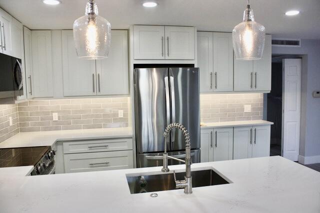 kitchen featuring backsplash, stainless steel appliances, sink, decorative light fixtures, and white cabinetry