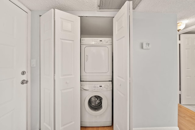 laundry area featuring stacked washing maching and dryer, a textured ceiling, and wood-type flooring