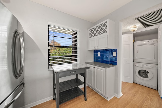 clothes washing area with light hardwood / wood-style flooring and stacked washing maching and dryer