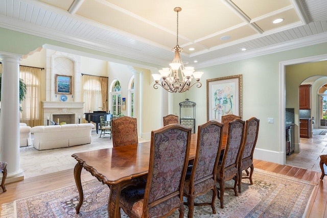 dining room featuring an inviting chandelier, light wood-type flooring, a fireplace, ornamental molding, and decorative columns