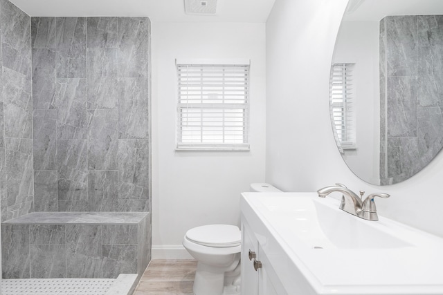 bathroom featuring vanity, toilet, wood-type flooring, and tiled shower