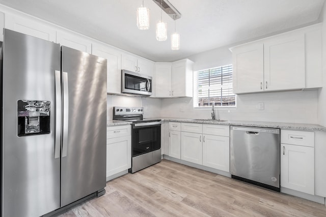 1609 N J Ter, Lake Worth, FL 33460 - kitchen with appliances with stainless steel finishes, white cabinets, light wood finished floors, light stone countertops, and hanging light fixtures