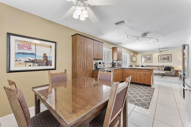 tiled dining room with a textured ceiling, track lighting, and ceiling fan