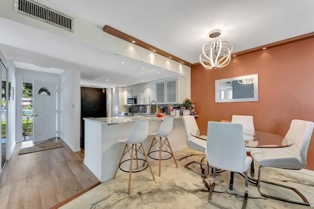 dining room with an inviting chandelier, sink, crown molding, and light hardwood / wood-style flooring