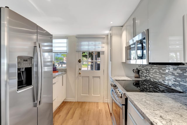 kitchen with decorative backsplash, modern cabinets, appliances with stainless steel finishes, light wood-type flooring, and white cabinetry