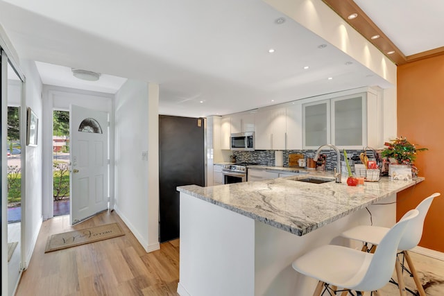 kitchen with appliances with stainless steel finishes, a breakfast bar, light stone counters, a peninsula, and a sink