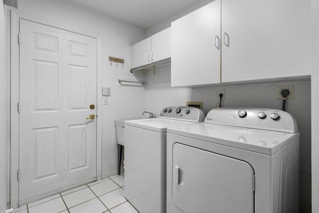 clothes washing area featuring washing machine and dryer, light tile patterned floors, and cabinets