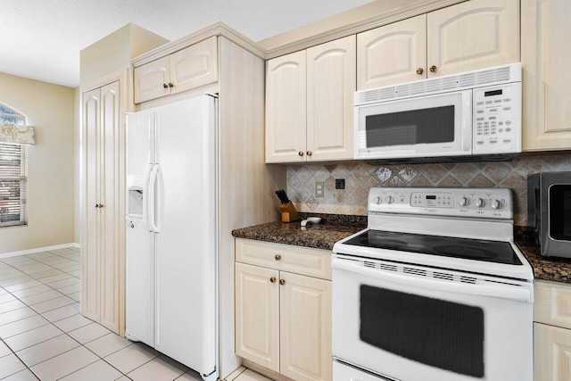 kitchen with dark stone countertops, decorative backsplash, light tile patterned floors, and white appliances