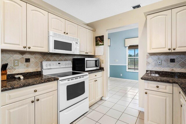 kitchen featuring dark stone countertops, white appliances, backsplash, and light tile patterned floors