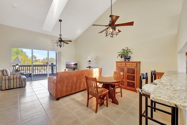 tiled dining space with ceiling fan, high vaulted ceiling, and a skylight