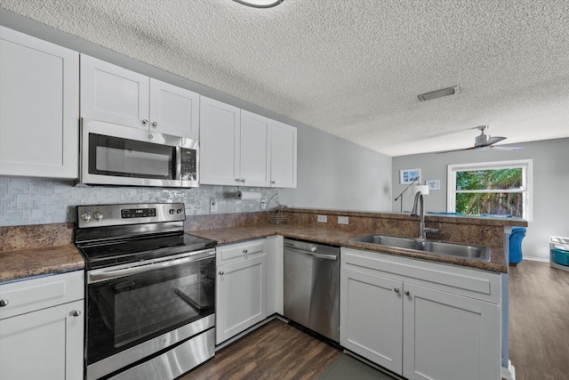 kitchen featuring kitchen peninsula, appliances with stainless steel finishes, sink, dark hardwood / wood-style floors, and white cabinetry