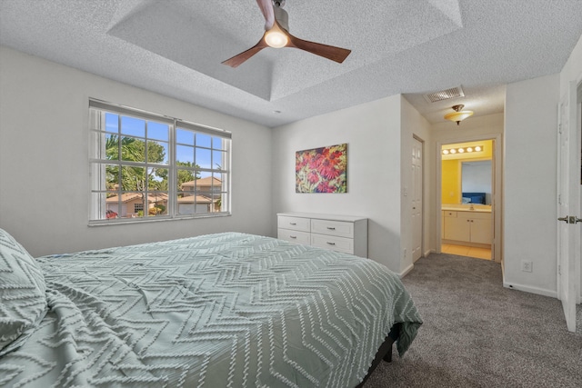 bedroom with ensuite bathroom, ceiling fan, a textured ceiling, a tray ceiling, and carpet floors