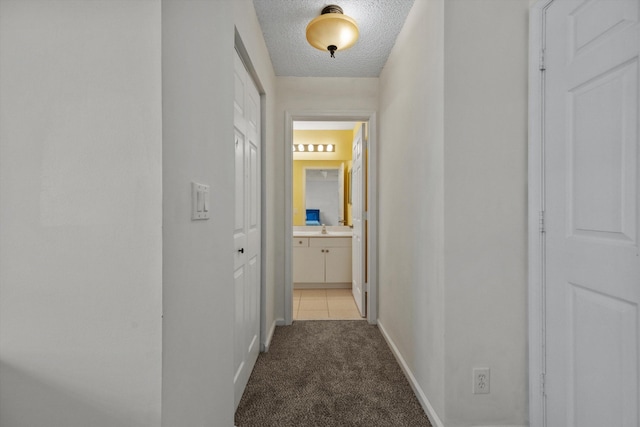 hall with a textured ceiling, light colored carpet, and sink