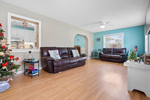 living room with a textured ceiling, ceiling fan, and light hardwood / wood-style floors