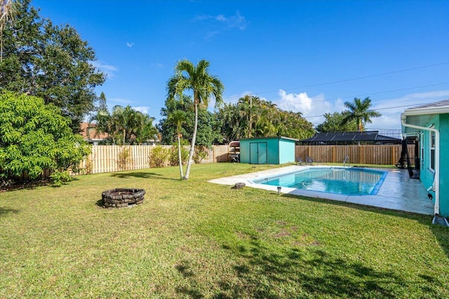 view of pool with a lawn, a fire pit, and a storage shed