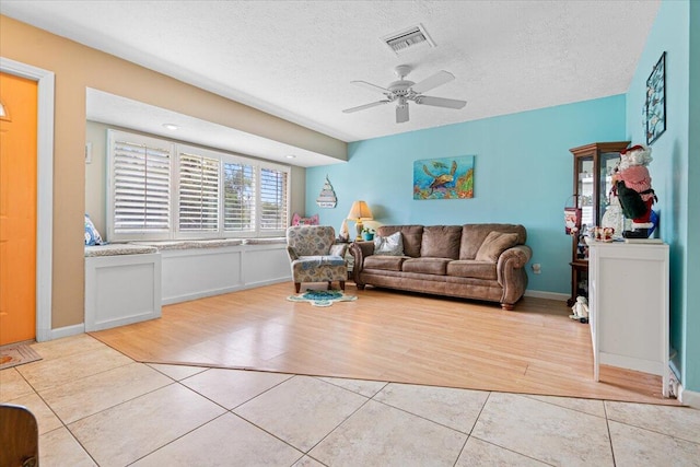 living room featuring light tile patterned flooring, a textured ceiling, and ceiling fan