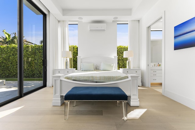 bedroom with access to exterior, light wood-type flooring, and a wall unit AC