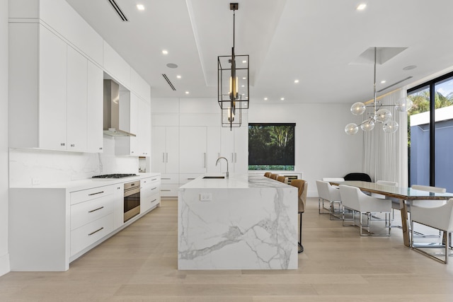 kitchen featuring appliances with stainless steel finishes, decorative light fixtures, wall chimney exhaust hood, and an island with sink