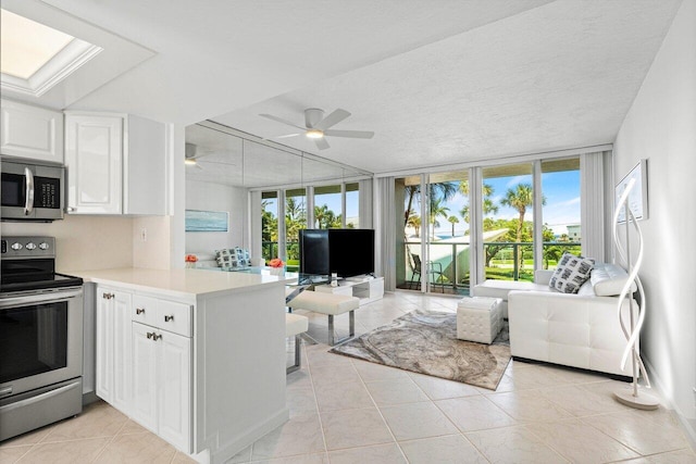 kitchen with kitchen peninsula, expansive windows, stainless steel appliances, light tile patterned floors, and white cabinets